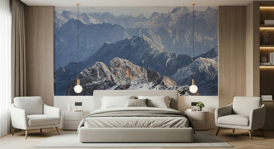 Ethereal Range wallpaper mural of hazy blue mountain peaks behind a grey bed flanked by two cream armchairs in a bedroom