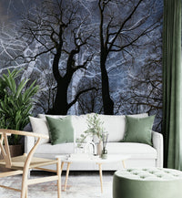 Ethereal Tree Silhouette wall mural of dark trees against a blue sky behind a white sofa with sage green pillows
