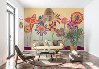Whimsical Fantasy Flowers wallpaper mural of bold flowers behind a rattan daybed sofa and potted olive tree in a living room