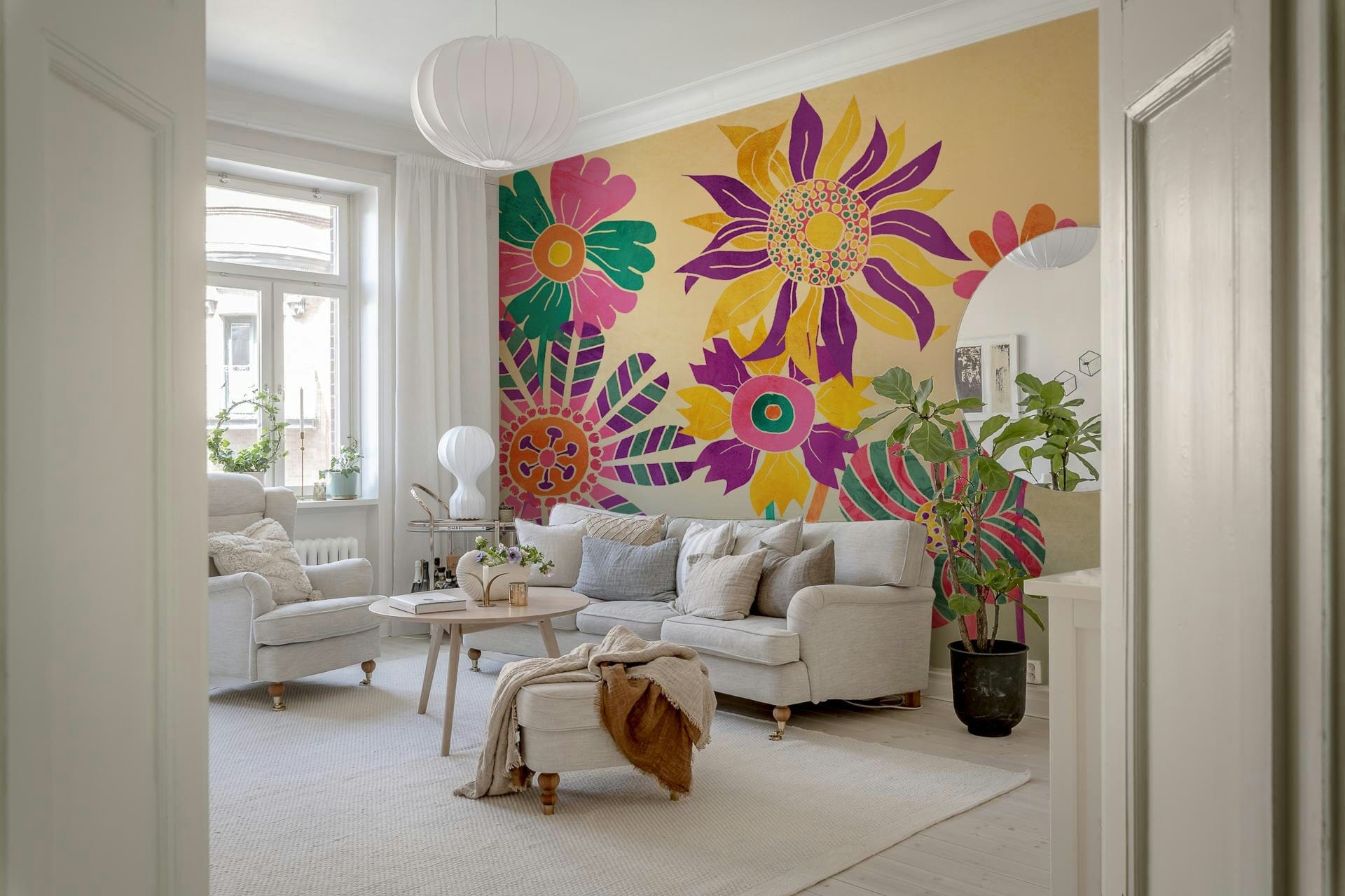 Whimsical Fantasy Flowers wallpaper mural in vivid pink and purple behind a cream sofa and armchair in a bright living room