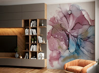 Fluid Dreamscape wallpaper mural of pink, blue and gold ink art beside a wood bookshelf and tan armchair in a living room