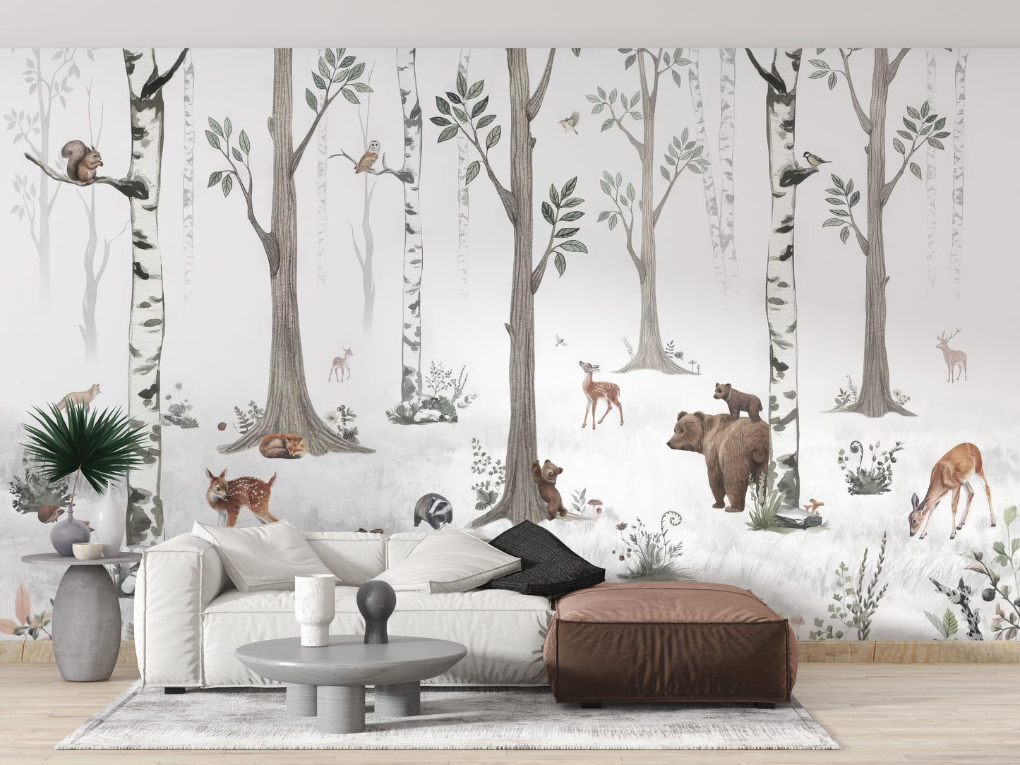 Forest Haven wallpaper mural of a watercolour birch forest with bear and deer behind a white sofa and leather ottoman in a living room