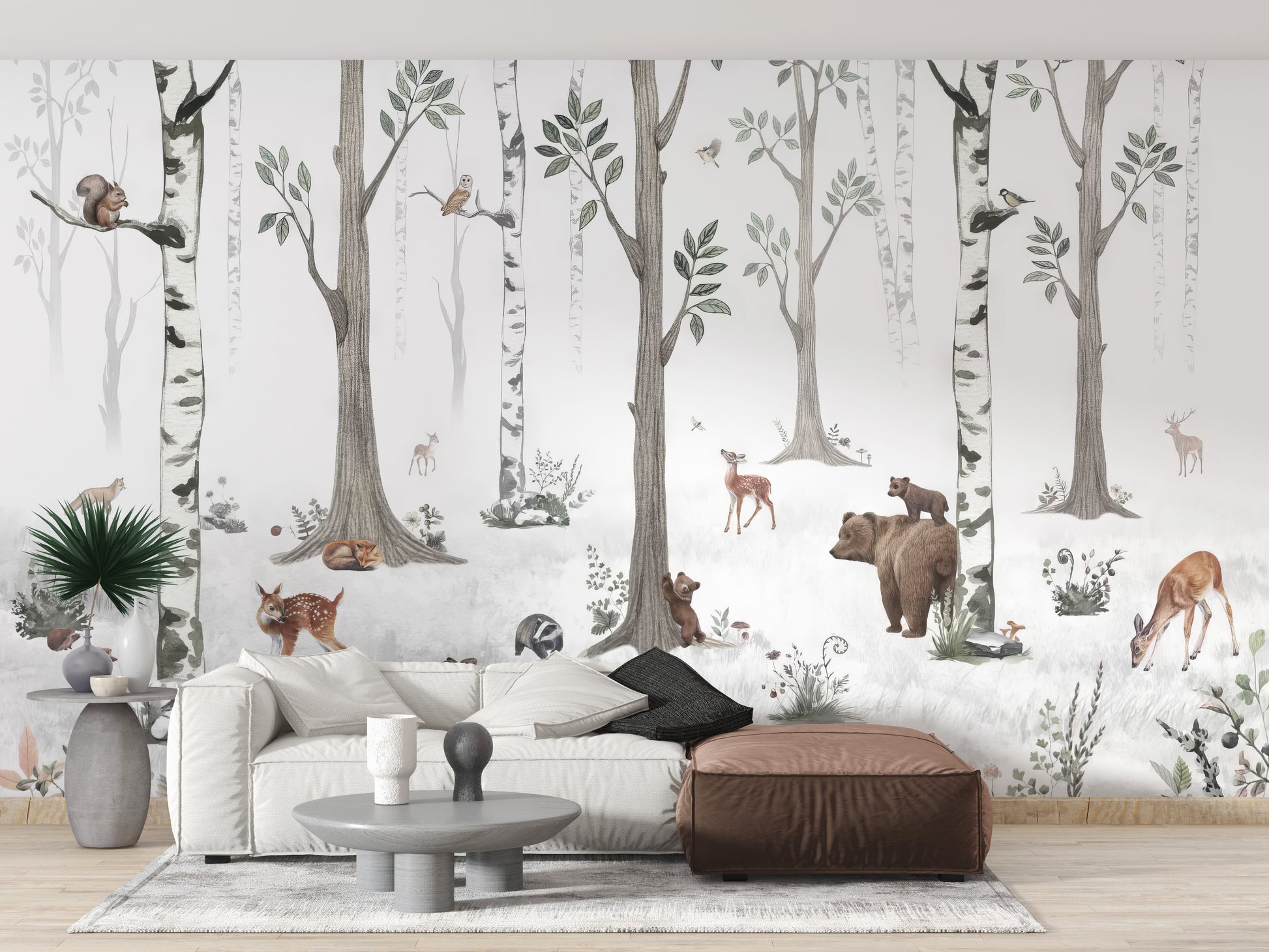 Forest Haven wallpaper mural of a watercolour birch forest with bear and deer behind a white sofa and leather ottoman in a living room