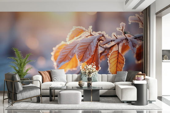 Gilded Frost wallpaper mural of frost-rimmed amber leaves behind a cream sofa and grey armchair in a living room