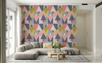 Geometric Forest Harmony wallpaper in pink and mustard triangles behind a grey sectional and wood table