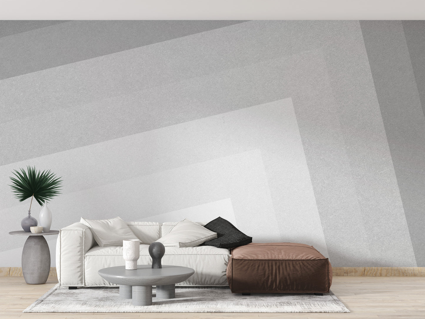 Geometric gray ombre layered wallpaper mural with angled tones behind a white sofa and leather ottoman in a living room