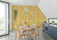 Golden Meadow Dream wallpaper in sunny yellow behind a round wood dining table beside blue kitchen units