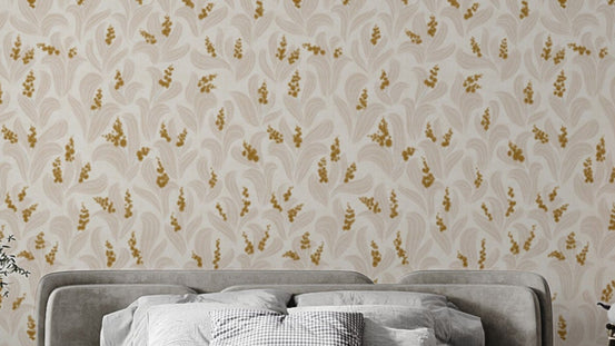 Golden Whispers Lily Valley wallpaper in cream with golden lily sprigs above a grey upholstered headboard in a bedroom