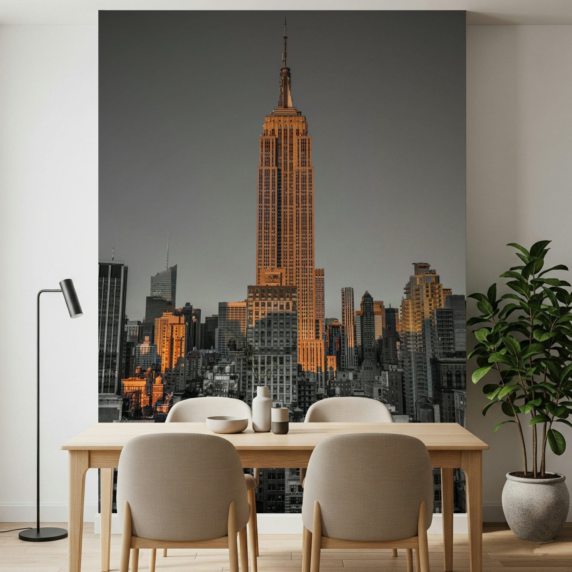 Gotham Gold wallpaper mural of the sunlit Empire State Building over grey Manhattan behind a wooden dining table with beige chairs
