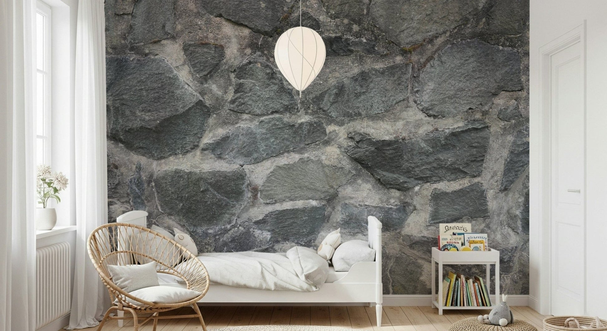 Granite Blocks wallpaper mural of grey stone behind a white bed and rattan chair in a bright kids room