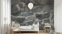 Granite Blocks wallpaper mural of grey stone behind a white bed and rattan chair in a bright kids room