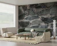 Granite Blocks wallpaper mural of grey stone behind a green sofa and cream boucle lounge chair in a living room