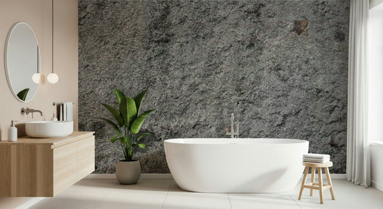 Granite Gray wallpaper mural behind a white freestanding tub, wood vanity and banana-leaf plant in a bathroom