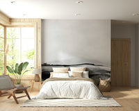 Grayscale Hills wallpaper mural in a boho bedroom with a white-bedded bed, woven leather chair and leafy plant