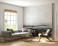 Grayscale Hills wallpaper mural in a sunny living room with a gray sofa and mid-century wooden armchair