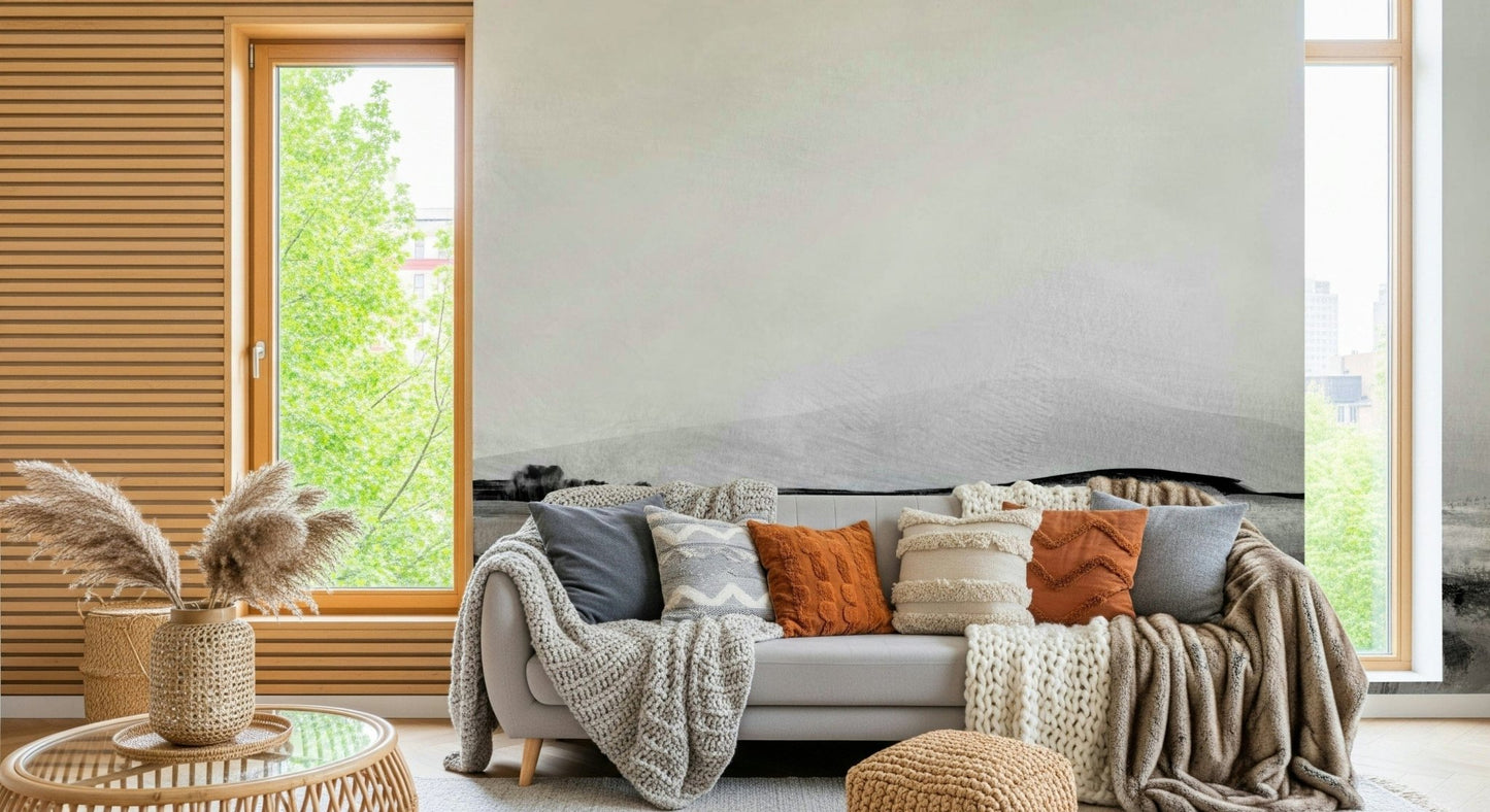 Grayscale Hills wallpaper mural behind a gray sofa piled with knit and terracotta cushions in a cozy room