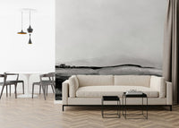 Grayscale Hills wallpaper mural behind a cream sofa in a minimalist living room with black nesting side tables