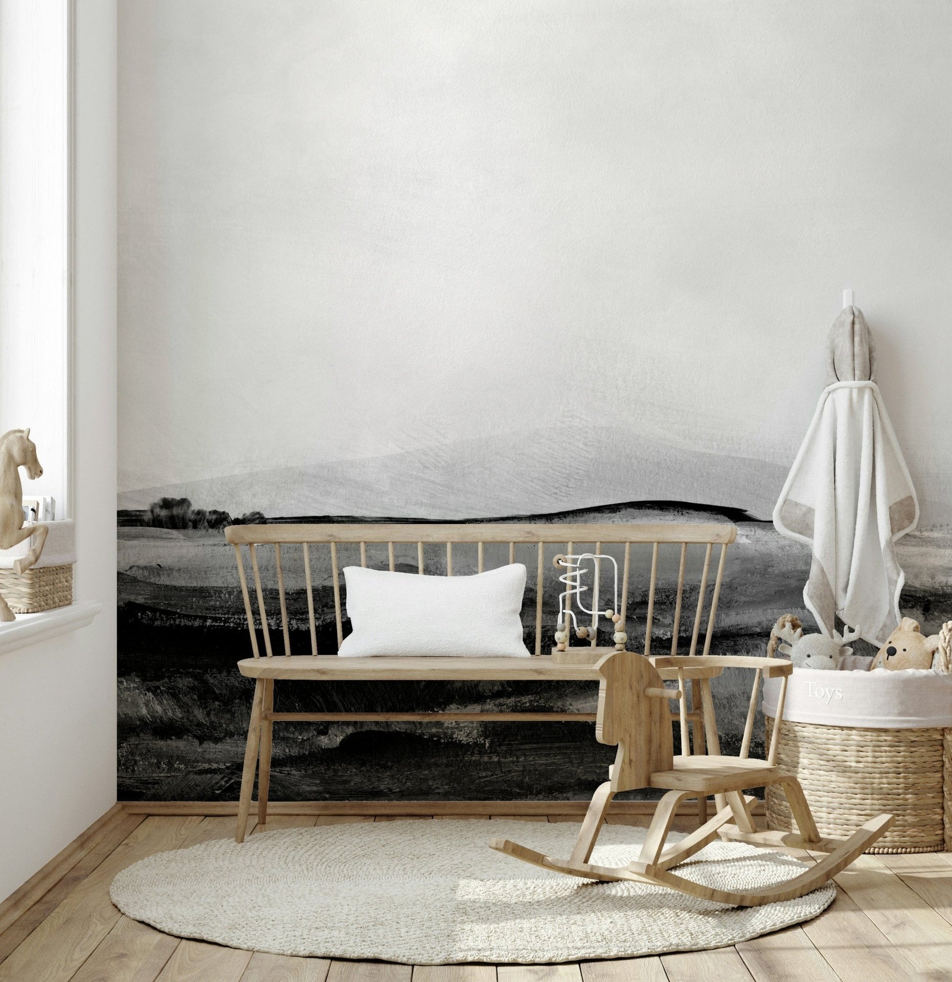 Grayscale Hills wallpaper mural in a nursery with a wooden bench, child rocking horse and woven toy basket