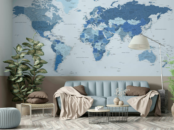 Highly Detailed World Map in Blue wallpaper mural behind a light-blue sofa with beige throws and a leafy plant in a living room