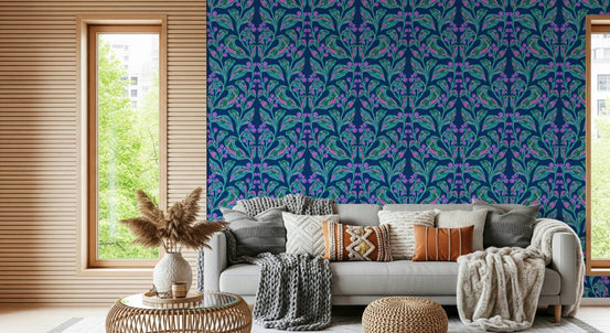 Indigo electric leaves wallpaper of teal and purple botanical motifs behind a grey sofa with knit cushions