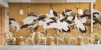 Japanese Flock Cranes wallpaper in ochre behind rattan chairs and woven tables in a cafe setting