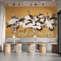 Japanese Flock Cranes wallpaper on a golden wall above white tables and rattan stools in a cafe