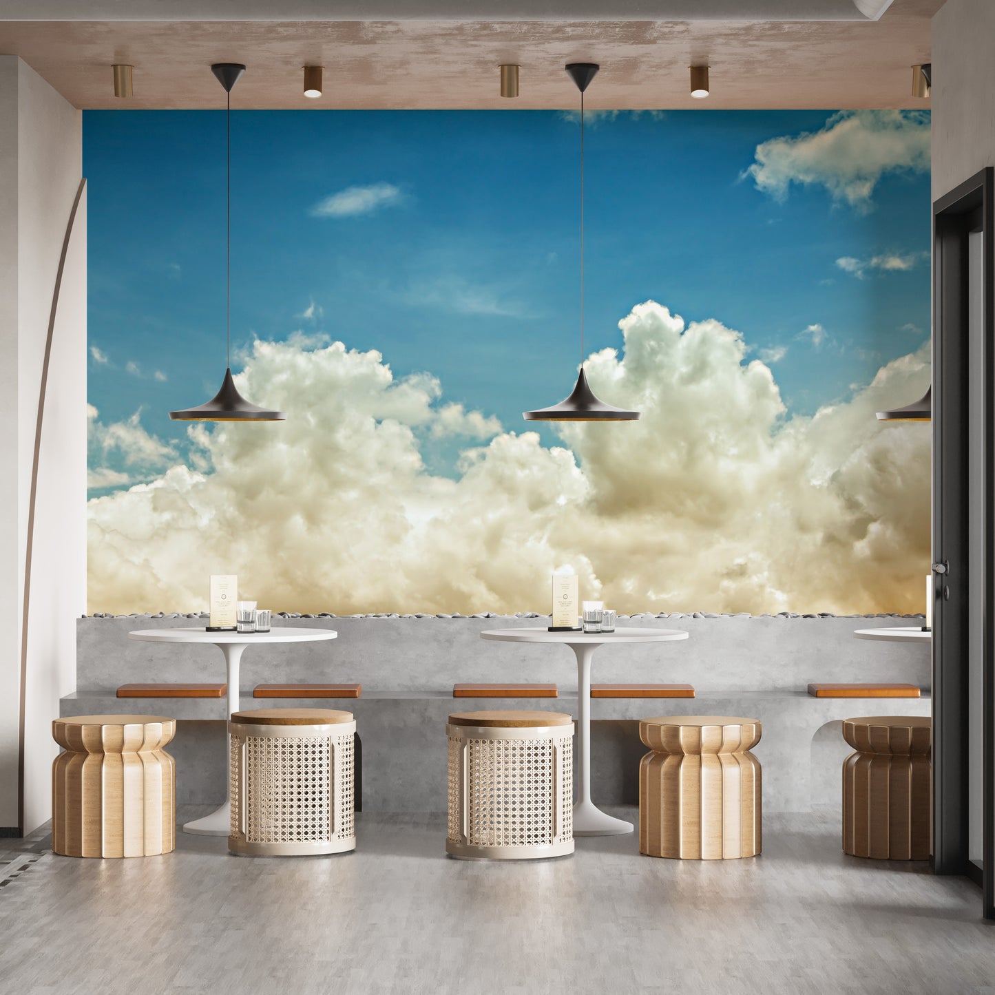 Light blue sky wallpaper mural of clouds above round white cafe tables with woven cane stools and bench seating
