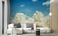 Light blue sky wallpaper mural with soft clouds behind a white sectional sofa and grey cushions in a living room