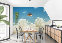 Light blue sky wallpaper mural of fluffy cream clouds behind a wood dining table and black bentwood chairs