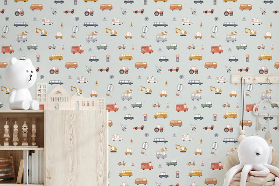 Little Transports in blue wallpaper mural in a nursery with a white teddy lamp and wooden console, soft sage cars and trucks