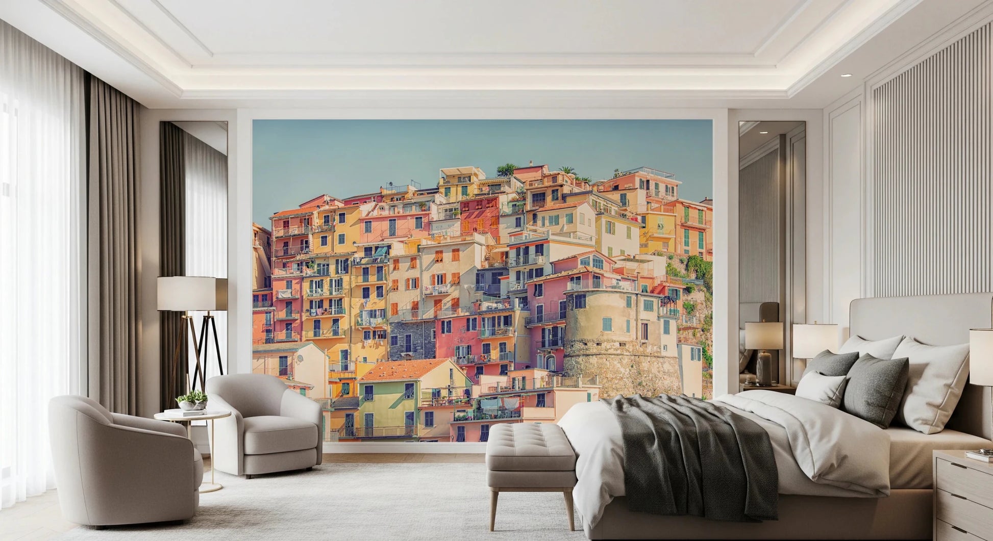 Manarola Vista wall mural of Italian hillside houses behind a beige bed and armchairs in a bedroom