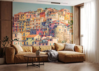 Manarola Vista wall mural of pastel hillside houses behind a camel leather sectional in a living room