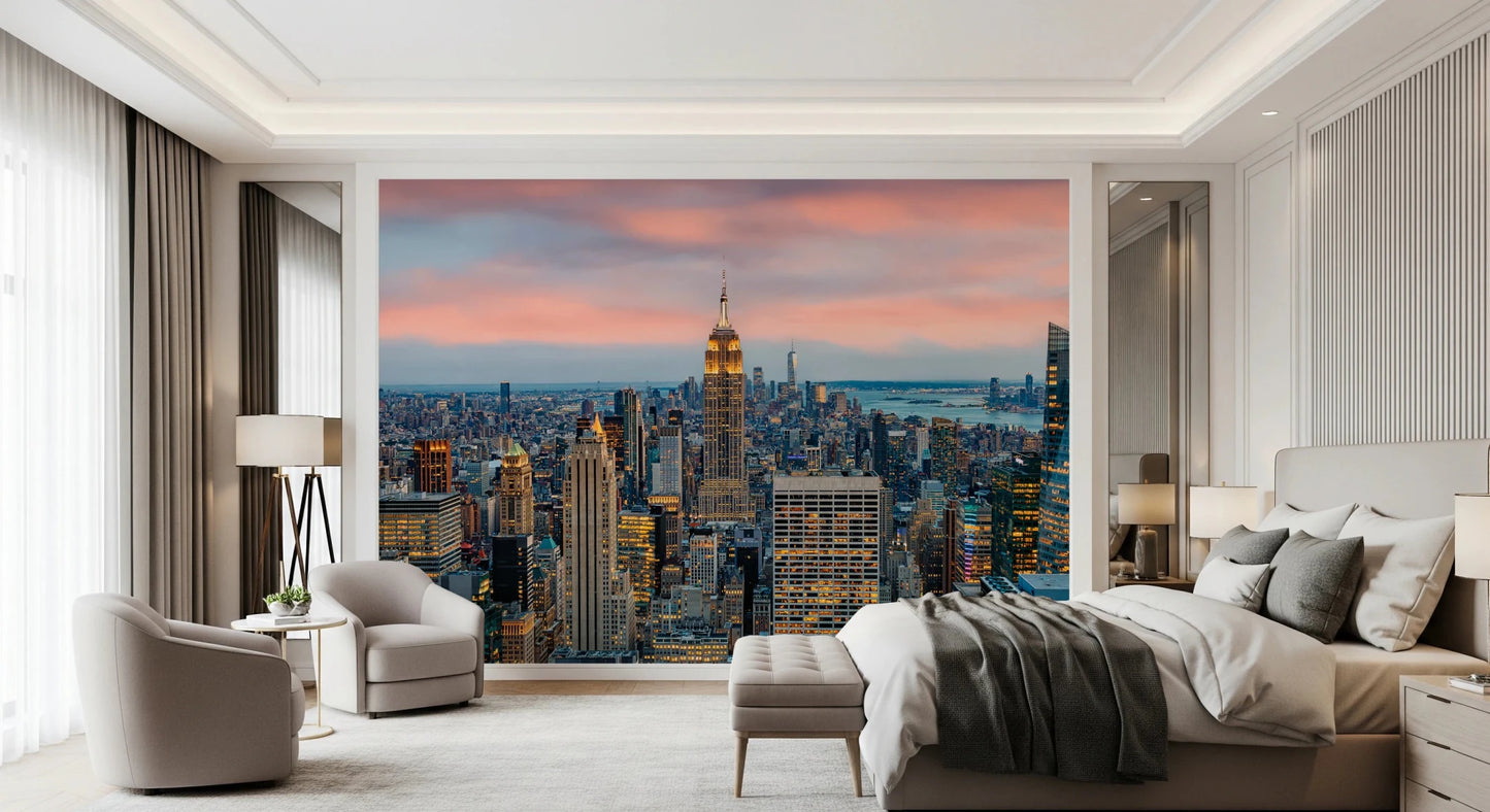 Manhattan Dawn wallpaper mural with a pink sunset sky behind a beige bed and two cream swivel chairs