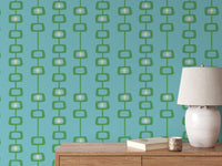 Mid Century Atomic Orbs wallpaper in green and teal behind a wood console with a cream ceramic lamp