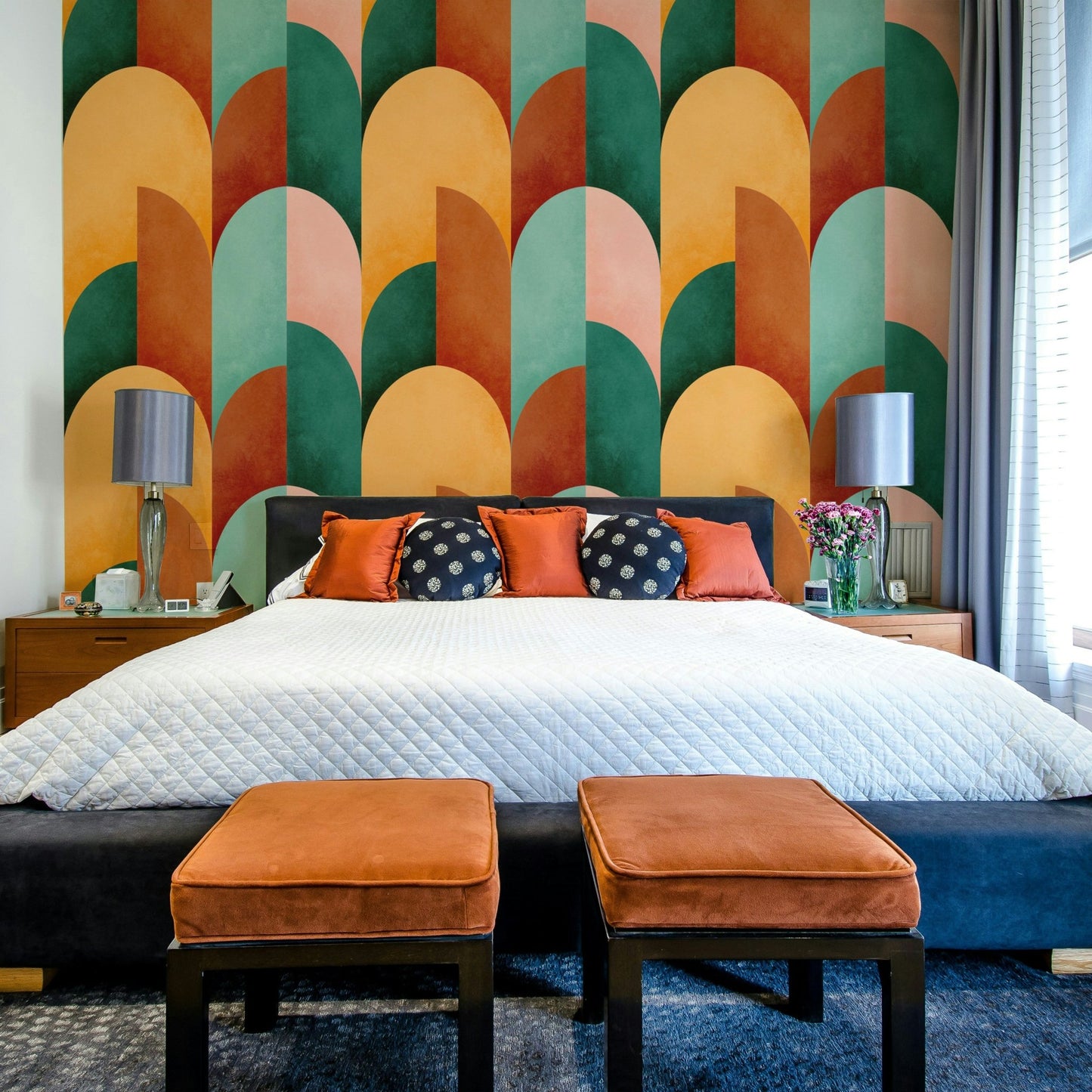 Mid Mod Geometry Sunburn wallpaper mural above a bed with navy polka-dot and rust pillows and orange velvet ottomans