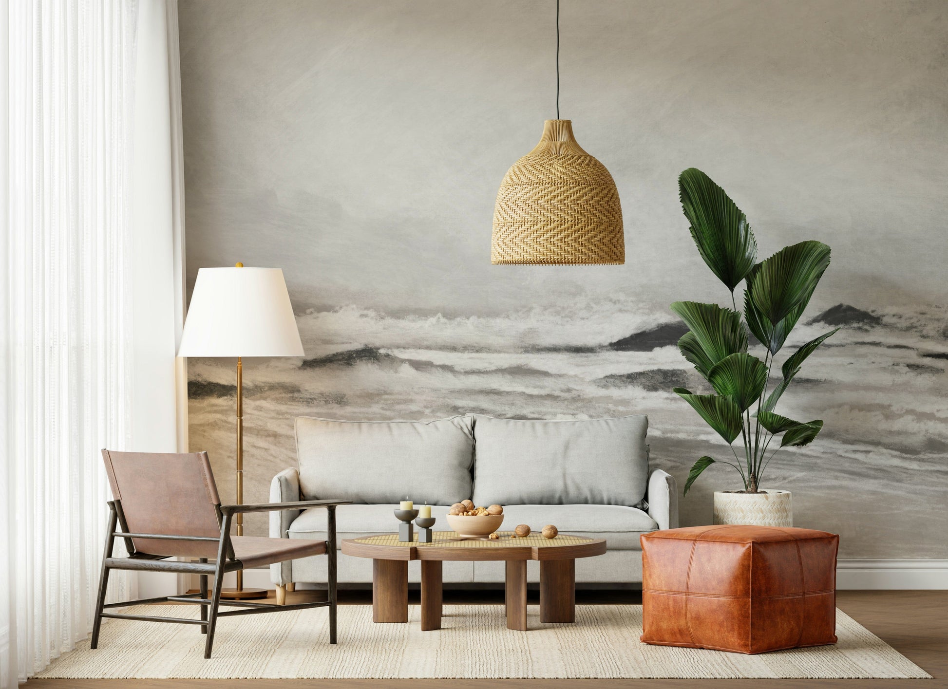 Misty Coast wallpaper mural in soft grey behind a grey sofa and terracotta leather pouf in a boho living room