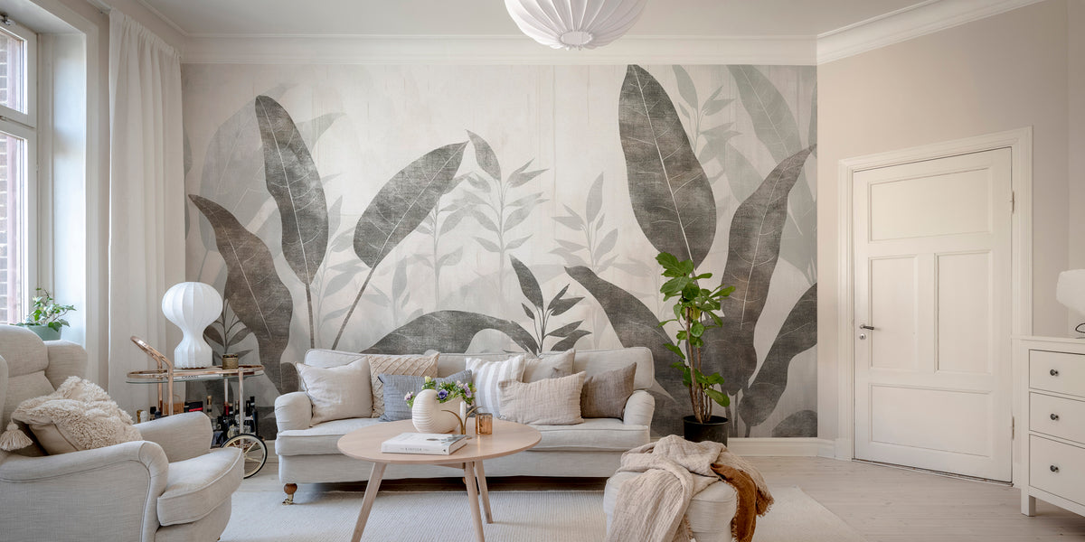 Monochrome Tropical Leaves wall mural behind a grey sofa and round wood table in a bright living room