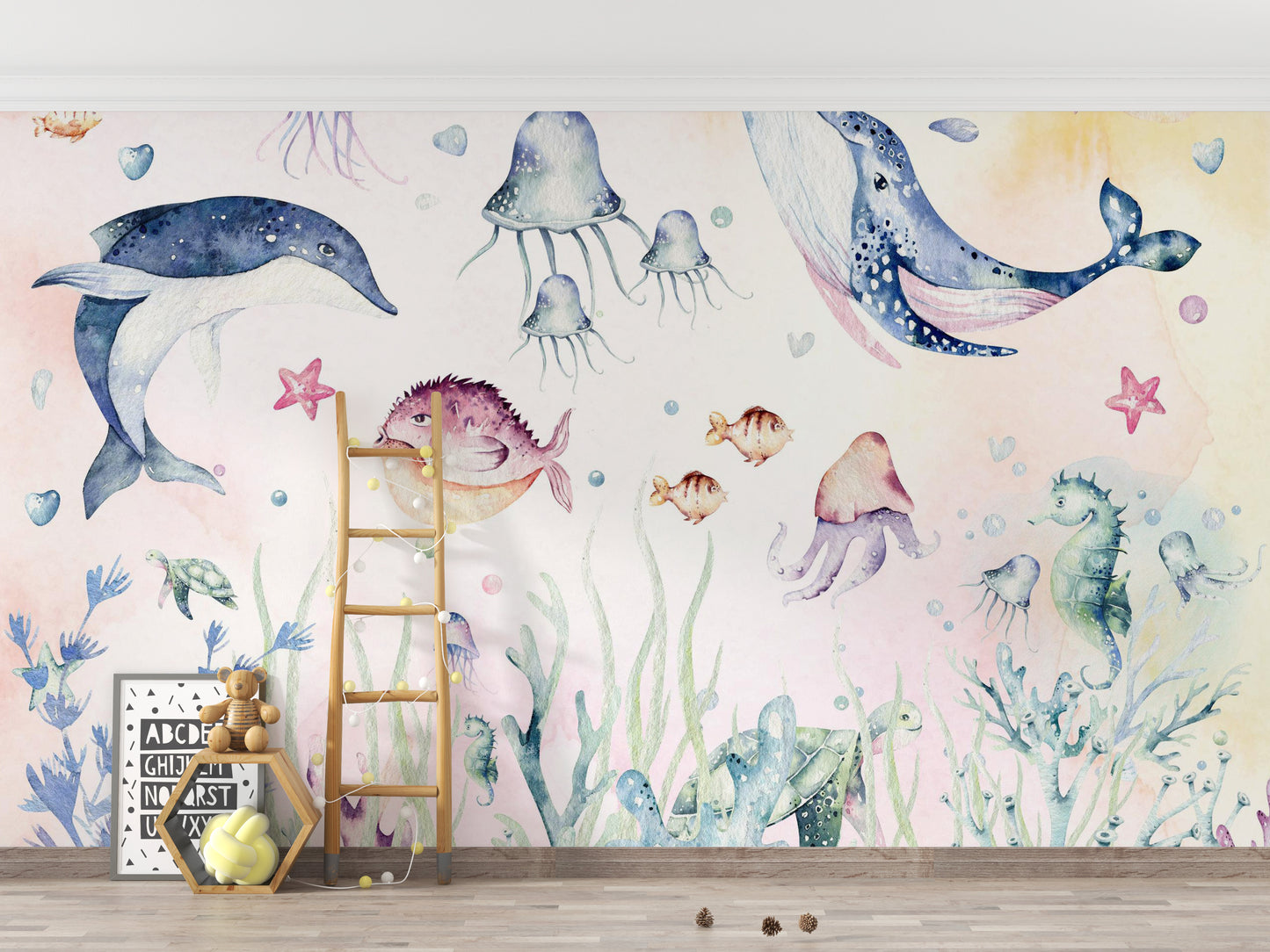 Nautical Creatures wall mural with watercolour whale and dolphin behind a wood ladder and teddy bear in a kids room