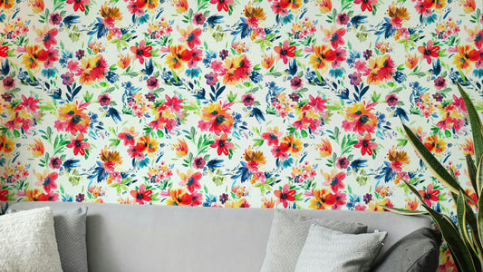Painterly Flowers Tropical Red wallpaper with vivid watercolor blooms behind a gray sofa and snake plant in a living room