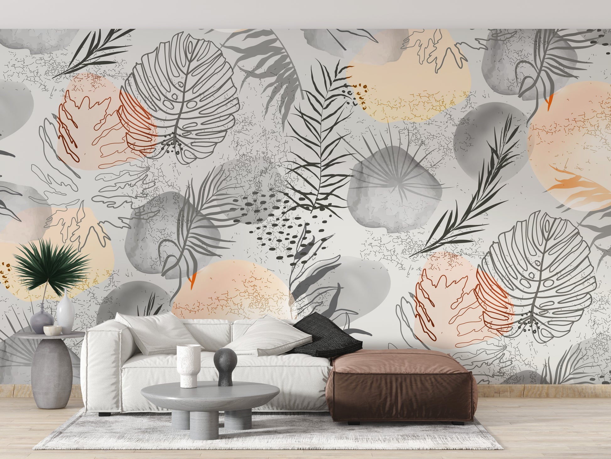 Palm tropical leaves wallpaper mural in neutral tones behind a white sofa and brown leather ottoman