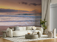 Peace at the Beach wallpaper mural of a sunset shoreline behind a cream curved sofa and round ottoman in a living room