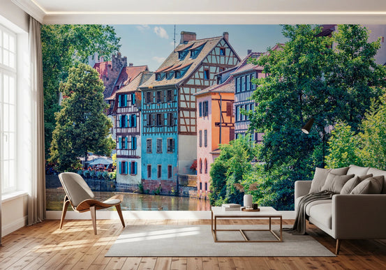 Petite France Charm wallpaper mural of colorful half-timbered canal houses behind a beige sofa and wood chair in a living room
