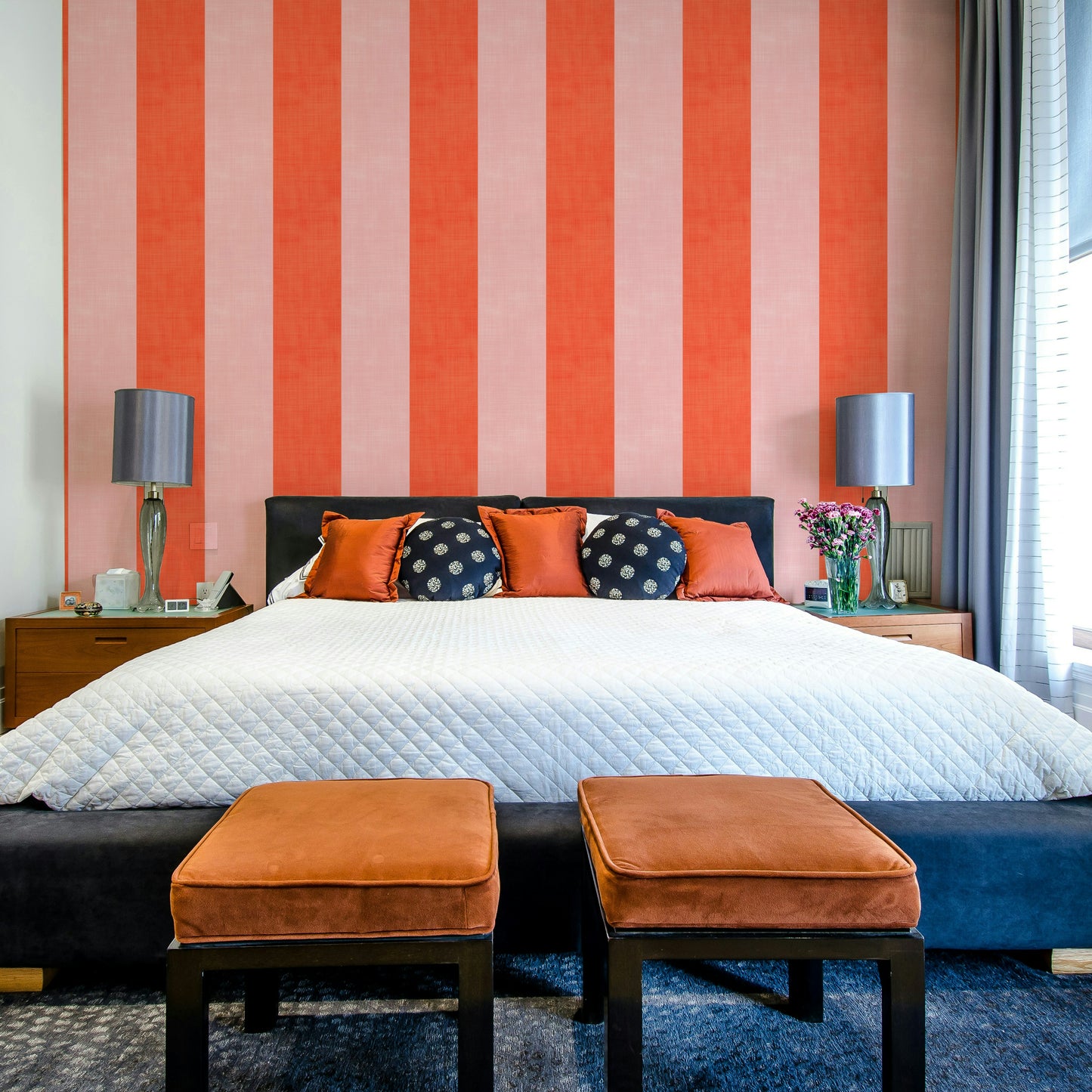 Pink and Red Stripes Linen Texture wallpaper behind a black bed with rust ottomans and table lamps
