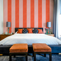 Pink and Red Stripes Linen Texture wallpaper behind a black bed with rust ottomans and table lamps