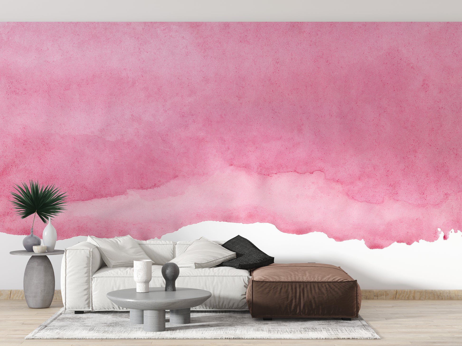 Pink shades watercolor wallpaper with a soft pink wash behind a white sofa and brown leather ottoman in a living room