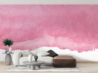 Pink shades watercolor wallpaper with a soft pink wash behind a white sofa and brown leather ottoman in a living room