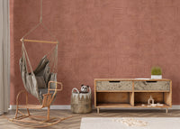 Mystic Terracotta wallpaper mural in warm clay tones behind a rattan hanging swing chair and wood credenza in a living room