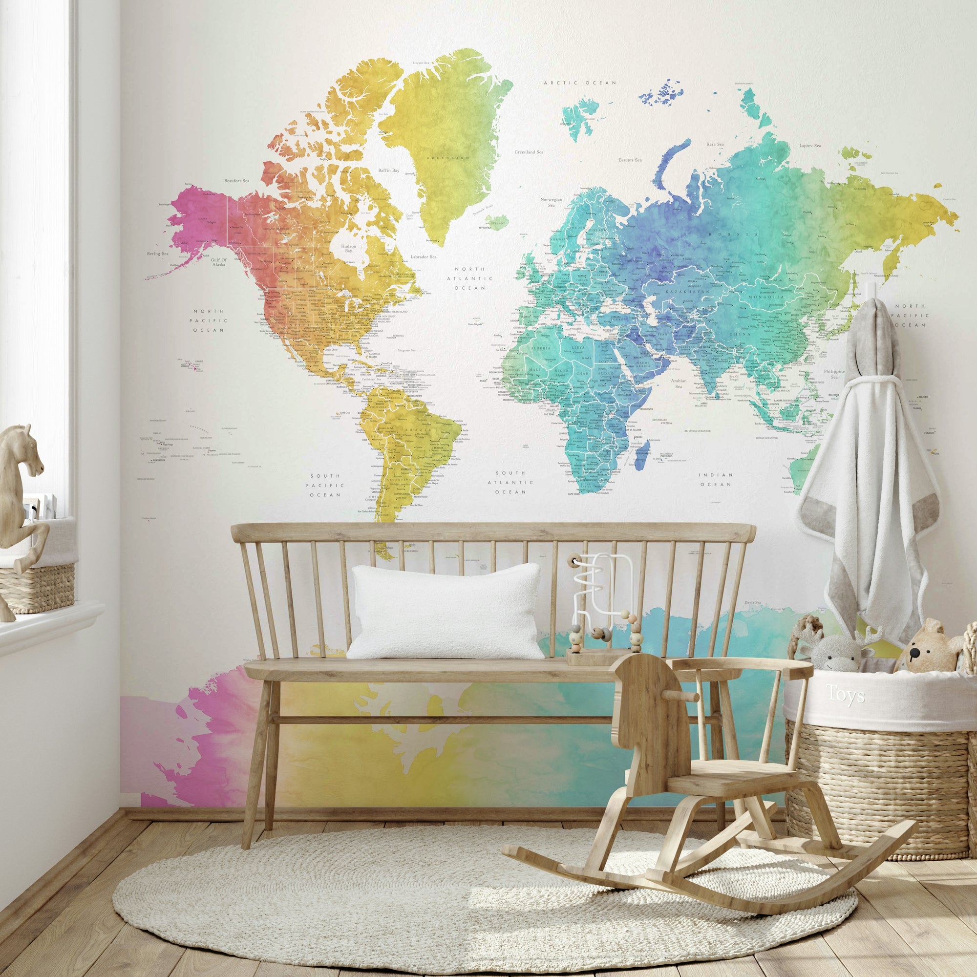Rainbow World Map wallpaper in rainbow watercolor behind a wooden bench and rocking horse with a toy basket in a nursery