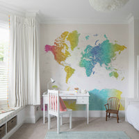 Rainbow World Map wallpaper in vivid watercolor behind a white desk and chair with a coral cushion in a girls bedroom