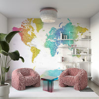 Rainbow World Map wallpaper in bright watercolor behind blush pink feathered armchairs and white shelves in a living room